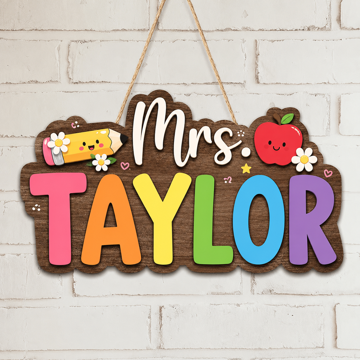 A personalized wooden hanging sign for a teacher, featuring the text 'Mrs. TAYLOR' in colorful letters on a brown wood background, with a smiling yellow pencil, red apple, and white flowers, hanging against a white brick wall.