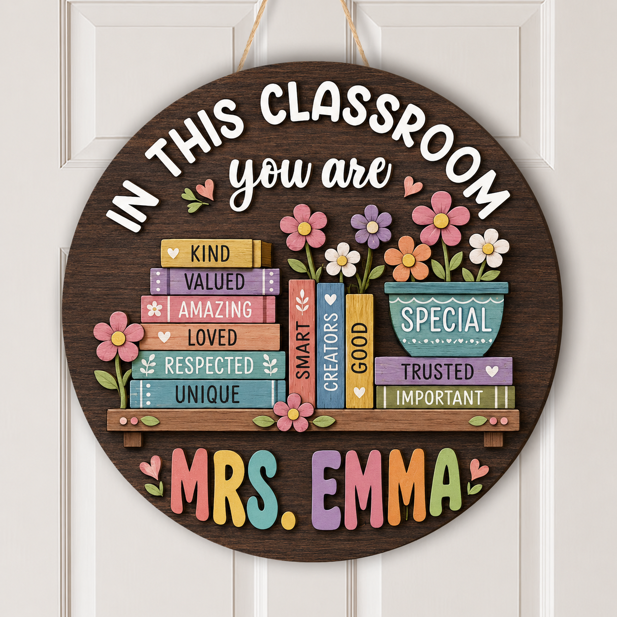 Personalized round wooden classroom door sign hanging on a white paneled door. The sign features a dark brown wood background with colorful decorative books, flowers, and the text 'IN THIS CLASSROOM you are MRS.
