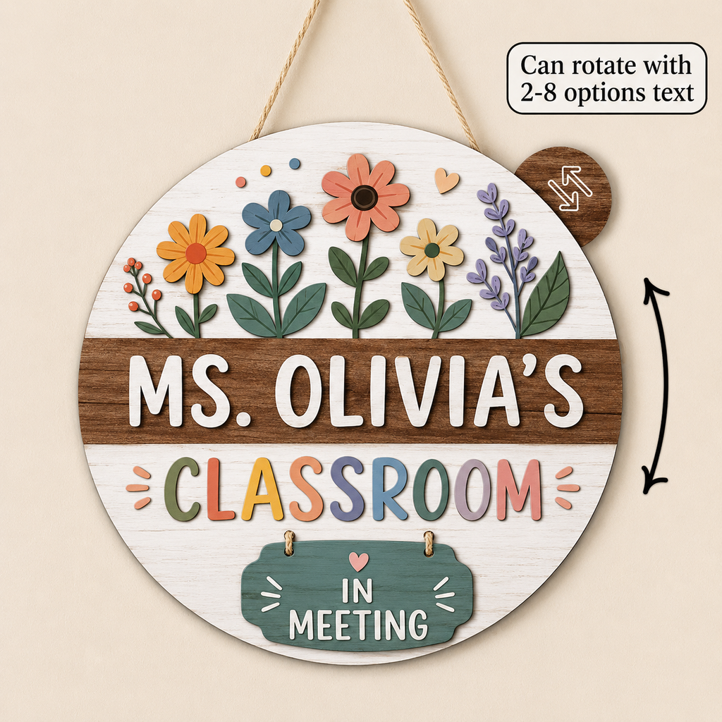 Personalized round wooden classroom sign hanging by a rope, with floral cutout details around the top and the text 'MS. OLIVIA'S CLASSROOM' and 'IN MEETING' in colorful lettering.
