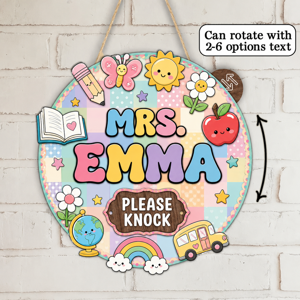 A round decorative hanging sign with the words “MRS. EMMA” in colorful letters and “PLEASE KNOCK” on a brown plaque, decorated with cute school-themed illustrations including a butterfly, sun, apple, pencil, book, globe, rainbow, clouds, and a yellow bus.